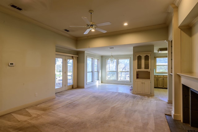 unfurnished living room with a tiled fireplace, light carpet, ceiling fan with notable chandelier, and ornamental molding