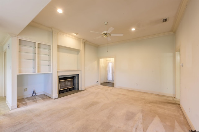 unfurnished living room featuring ornamental molding, light colored carpet, ceiling fan, built in features, and a tiled fireplace