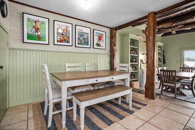 dining space with light tile patterned floors, a wainscoted wall, a textured ceiling, and ornamental molding