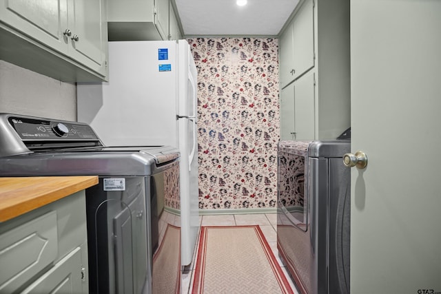 clothes washing area with cabinet space, light tile patterned flooring, and washer and clothes dryer