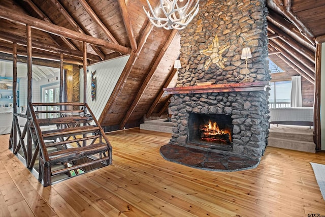 unfurnished living room featuring hardwood / wood-style floors, vaulted ceiling with beams, a stone fireplace, stairs, and wooden ceiling