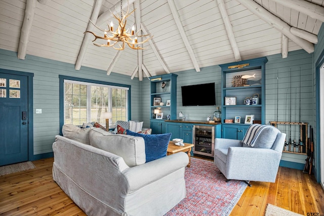 living room with lofted ceiling with beams, wine cooler, an inviting chandelier, and light wood-style flooring