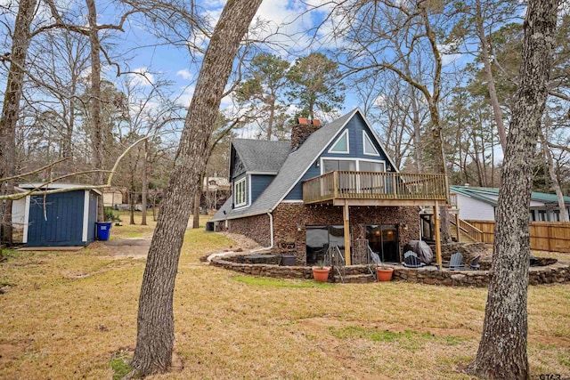 back of house featuring an outbuilding, a shed, a wooden deck, a chimney, and a lawn