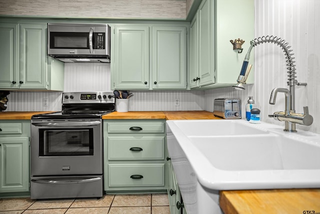 kitchen with butcher block countertops, green cabinetry, light tile patterned floors, stainless steel appliances, and a sink