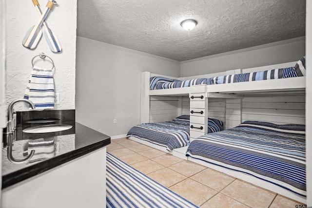 bedroom with tile patterned flooring, a textured ceiling, baseboards, and a sink