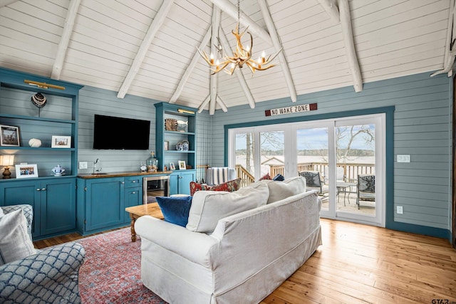 living area featuring wet bar, lofted ceiling with beams, light wood finished floors, and an inviting chandelier