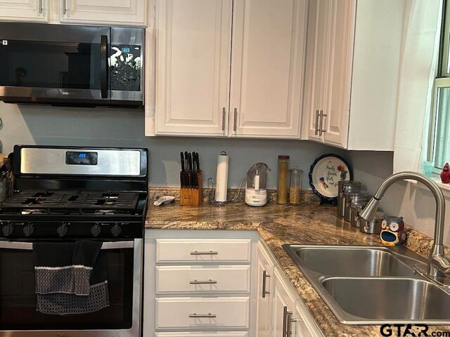 kitchen with dark stone countertops, white cabinetry, sink, and stainless steel appliances