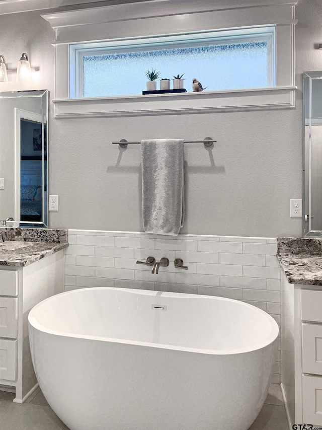9035 Shallow Cv, Tyler, TX 75703 - bathroom featuring tile walls, two vanities, a freestanding tub, plenty of natural light, and a wainscoted wall