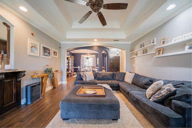 living room featuring ceiling fan with notable chandelier, dark wood-type flooring, crown molding, and a tray ceiling