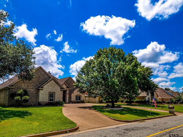 view of front of home with stone siding, curved driveway, a chimney, and a front yard