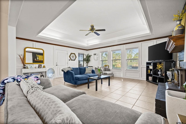 tiled living room with ceiling fan and a tray ceiling