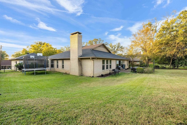 back of property featuring a trampoline and a lawn