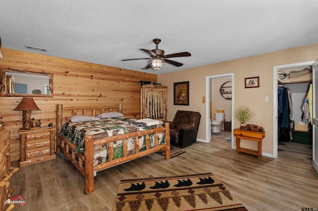 bedroom featuring a textured ceiling, visible vents, a walk in closet, and wood finished floors