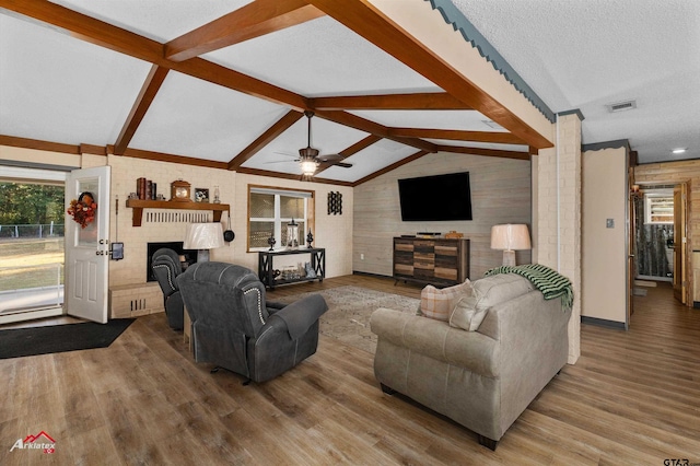 living room with lofted ceiling with beams, a brick fireplace, visible vents, and wood finished floors