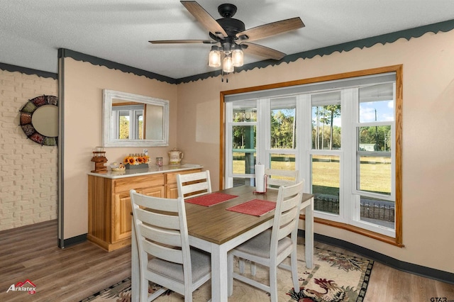 dining room with light wood-style floors, ceiling fan, a textured ceiling, brick wall, and baseboards