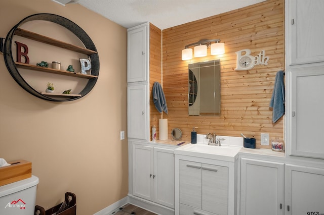 bathroom featuring toilet, wooden walls, vanity, and a textured ceiling