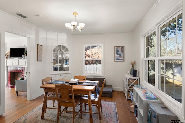 dining room with crown molding, wood-type flooring, a chandelier, and a brick fireplace