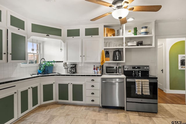 kitchen with appliances with stainless steel finishes, sink, white cabinets, backsplash, and ceiling fan