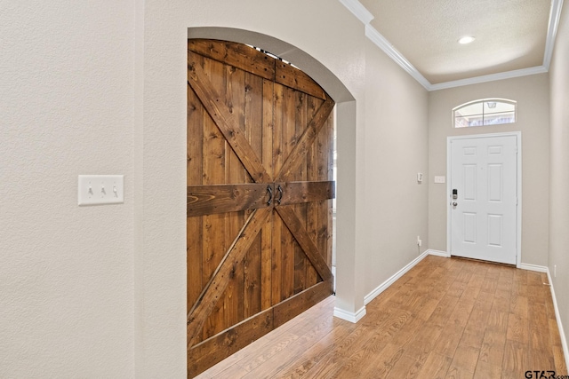 entryway with a textured ceiling, a barn door, crown molding, and light hardwood / wood-style flooring