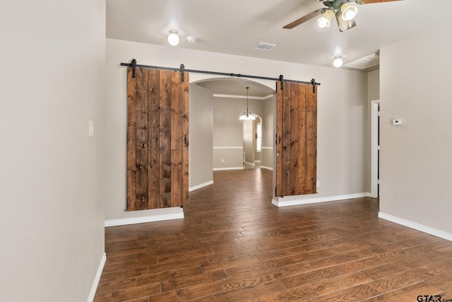 empty room featuring ceiling fan, dark hardwood / wood-style floors, and a barn door