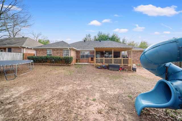 back of house with brick siding, a shingled roof, a trampoline, and fence