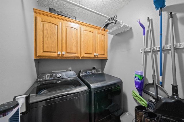 clothes washing area with separate washer and dryer, a textured ceiling, and cabinet space