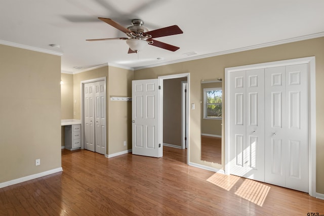 unfurnished bedroom featuring crown molding, multiple closets, hardwood / wood-style flooring, and ceiling fan