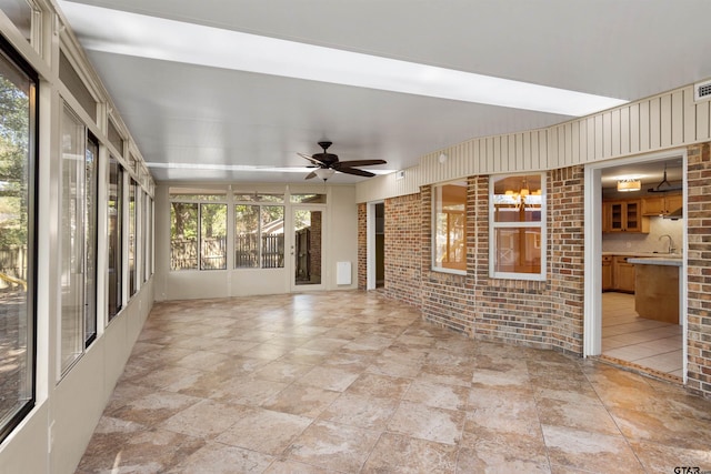 unfurnished sunroom with ceiling fan with notable chandelier and sink