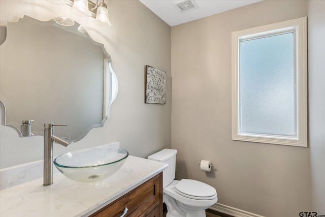 half bathroom featuring baseboards, visible vents, vanity, and toilet