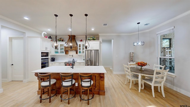 kitchen featuring light wood-type flooring, a kitchen island with sink, white cabinets, stainless steel fridge with ice dispenser, and pendant lighting