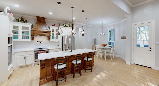 kitchen featuring premium range hood, stainless steel appliances, light hardwood / wood-style floors, white cabinets, and a kitchen island with sink