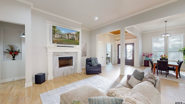 living room with light wood-type flooring, crown molding, a high end fireplace, and an inviting chandelier