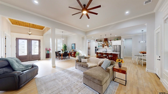 living room with ornamental molding, french doors, light hardwood / wood-style flooring, and ceiling fan with notable chandelier