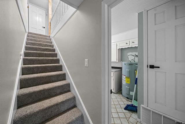stairway with baseboards, tile patterned floors, and electric water heater