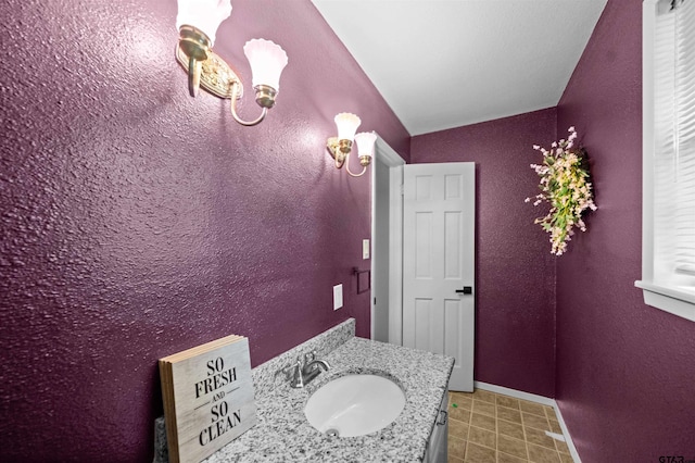 bathroom featuring a textured wall, vaulted ceiling, and vanity