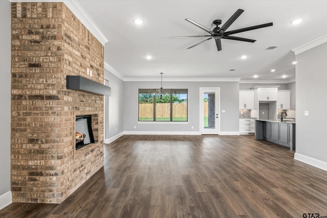 unfurnished living room featuring sink, ornamental molding, ceiling fan, a fireplace, and dark hardwood / wood-style flooring