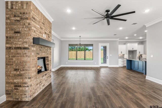 unfurnished living room with sink, ceiling fan, dark hardwood / wood-style floors, crown molding, and a brick fireplace