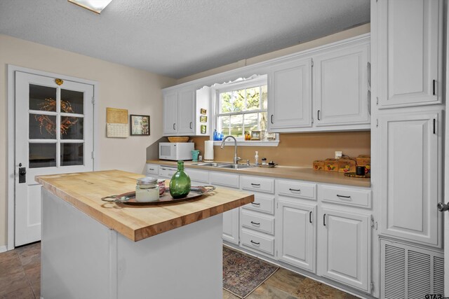 kitchen with butcher block countertops, white microwave, a sink, and white cabinetry