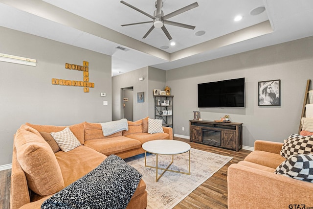 living room with a tray ceiling, baseboards, visible vents, ceiling fan, and wood finished floors