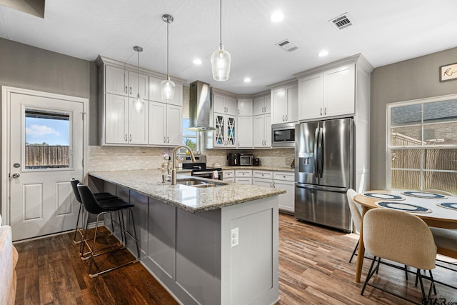 kitchen featuring a sink, visible vents, wall chimney range hood, a peninsula, and appliances with stainless steel finishes