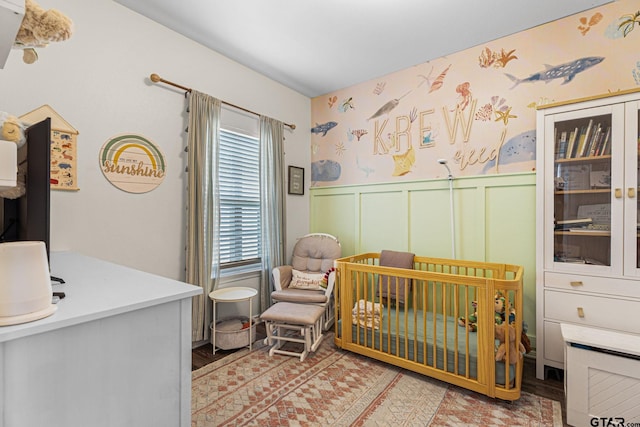 bedroom featuring wallpapered walls, a wainscoted wall, and a crib