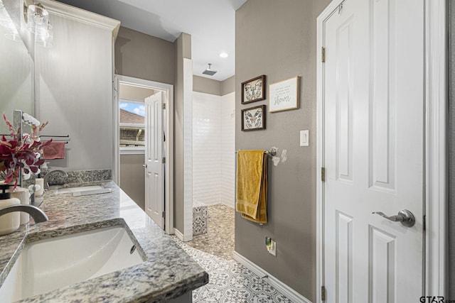 bathroom featuring double vanity, a sink, baseboards, and tiled shower