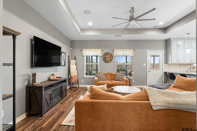 living room with visible vents, baseboards, a ceiling fan, dark wood finished floors, and a raised ceiling