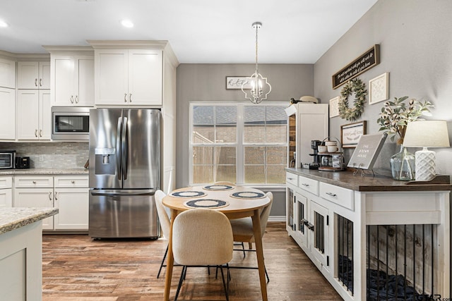 kitchen with wood finished floors, tasteful backsplash, appliances with stainless steel finishes, hanging light fixtures, and an inviting chandelier