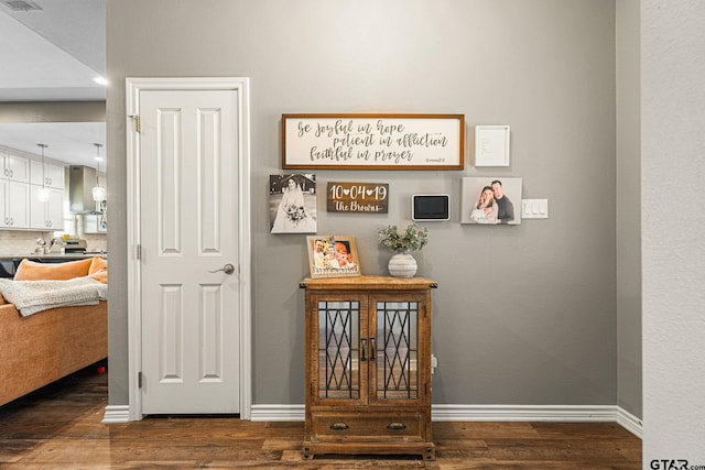 interior space with wood finished floors, visible vents, baseboards, and wall chimney exhaust hood