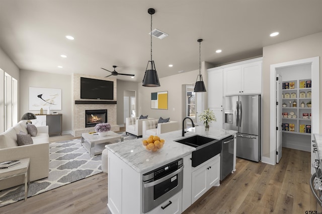 kitchen with sink, stainless steel appliances, light stone counters, white cabinets, and a center island with sink