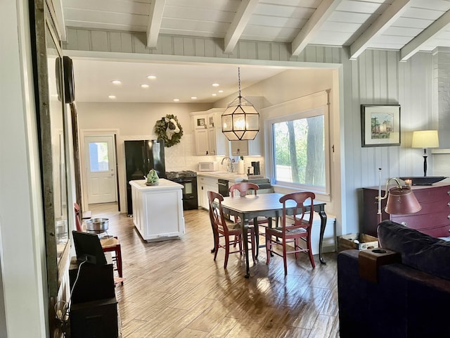 dining area featuring beamed ceiling, sink, light wood-type flooring, and wood walls