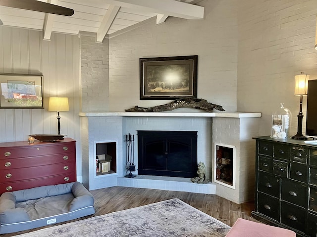 living room featuring wooden ceiling, wood-type flooring, a brick fireplace, and vaulted ceiling with beams