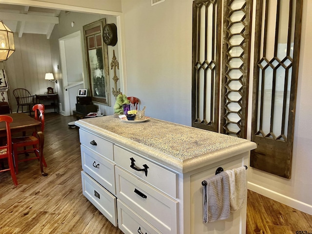 kitchen featuring beamed ceiling, light hardwood / wood-style floors, and white cabinets