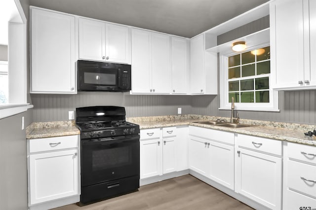 kitchen featuring light wood-type flooring, black appliances, light stone countertops, sink, and white cabinets